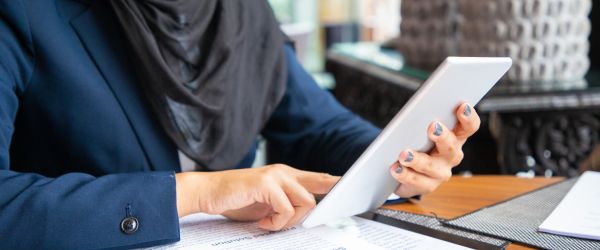 Businesswoman reading contract and consulting internet. Young Muslim business woman sitting in cafe, reading papers and using tablet. Digital communication concept