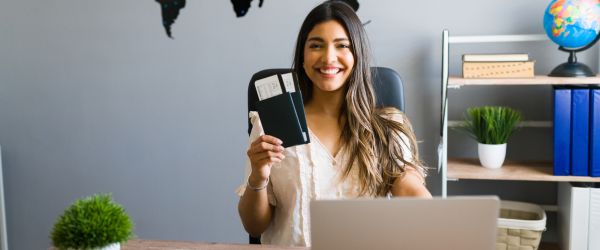 Portrait of a travel agent booking a flight I am here to help you with your booking and travel questions. Female sales agent holding plane tickets while smiling and making eye contact at the travel agency