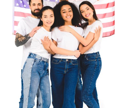 multicultural group of young people smiling and hugging while holding flag of usa isolated on white