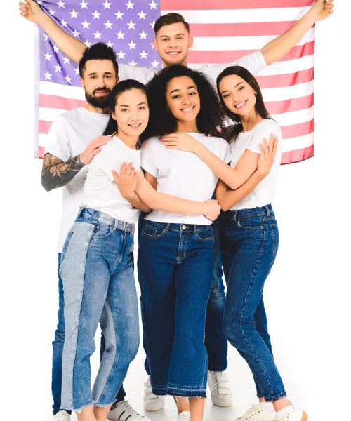 multicultural group of young people smiling and hugging while holding flag of usa isolated on white