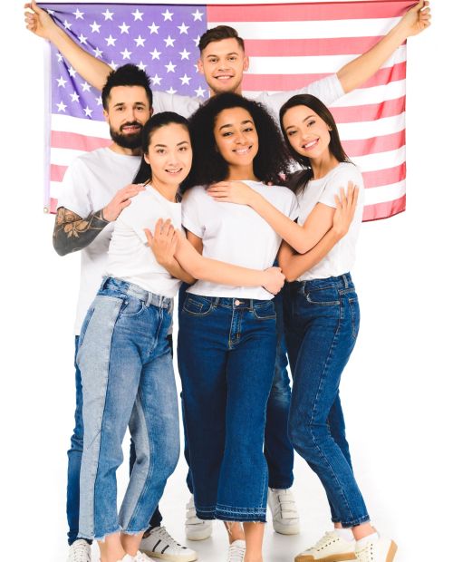 multicultural group of young people smiling and hugging while holding flag of usa isolated on white