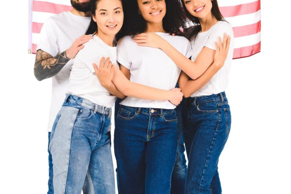 multicultural group of young people smiling and hugging while holding flag of usa isolated on white